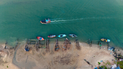 Aerial view of fisherman's boat was moored along the shore, and a boat was moving in the sea on the blue water surface.