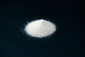 Fototapeta premium close-up on a black-blue background white crumbly granulated sugar lies on it, crystal lumps around a pile of sugar are harmful to health