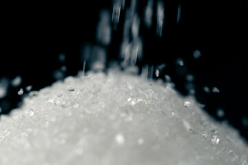 close-up on black-and-blue background lies on white crumbly granulated sugar crystals on top pour...