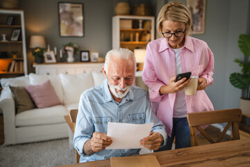 senior man read a document from envelope and woman use cellphone