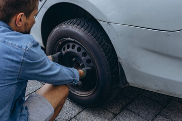 Young man in unscrewing lug nuts on car wheel in process of new tire replacement,using wrench while changing flat tire on the road.