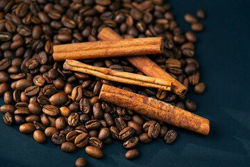 top shot close-up on a black and blue background roasted coffee beans lie laid out on a background with several cinnamon sticks spicy coffee popular recipe