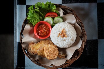 Fried chicken rice and tempeh with mustard greens and chili sauce on a rattan plate, ready to eat