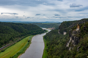 A river flows through a lush green valley with a train passing by. The scene is serene and...