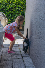 funny friends: little girl, five years old child sitting on the ground and black cat, on the street in Summertime