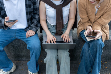 Fototapeta premium Three people sitting on a bench with a laptop and cell phones