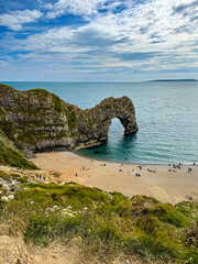 Hot summer day at Durdle Door. Durdle Door limestone arch on the Jurassic Coast in Dorset.Natural landmark.Summer holidays England. Crowded beach, people are spending summer weekend in English seaside