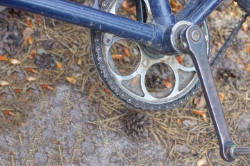 a black metal pedal with an asterisk and a chain on the iron frame of an old bicycle lies on gray earth on the street