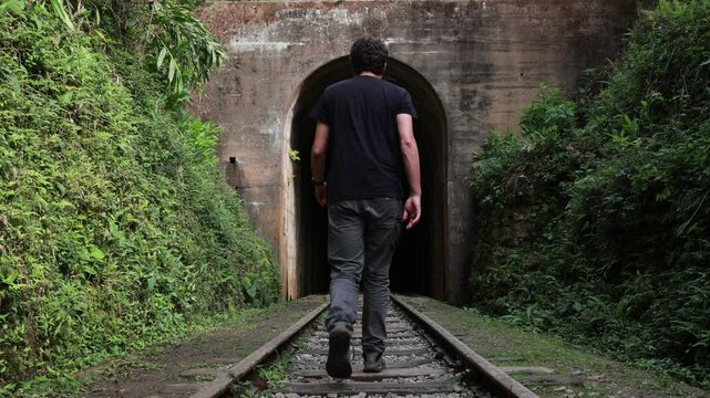 Homem caminhando estrada de ferro em dire&ccedil;&atilde;o ao t&uacute;nel escuro