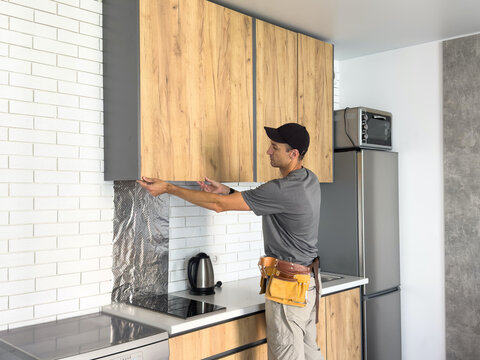 The carpenter finalizing the assembly of the kitchen shelf on the wall.
