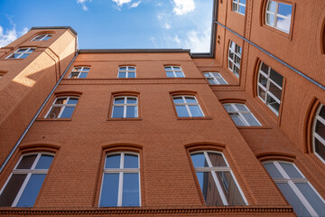 A brick building with many windows and a blue sky in the background. The building is tall and has a lot of windows