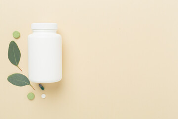 Bottle with pills and green leaves on color background, top view