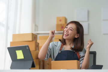 Excited woman celebrating success while preparing packages, working from home. Home business, e-commerce, and small business concept.