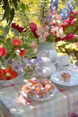 Still life of table set with flowers, fruit and cakes for afternoon tea outside in a garden in summer