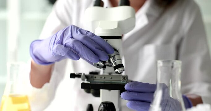 Medic worker in rubber gloves adjusts electronic microscope sitting at table. Woman prepares equipment for sample examination in laboratory slow motion