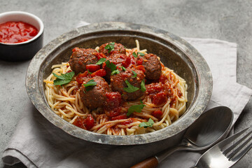 Delicious spaghetti with meatballs and tomato sauce on a rustic table with neatly arranged cutlery and napkin, Italian cuisine