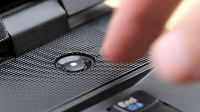 Man's finger reaching to press a generic laptop computer power button, about to turn the device on or off, hovering over the power key, object closeup detail, one person, simple abstract concept
