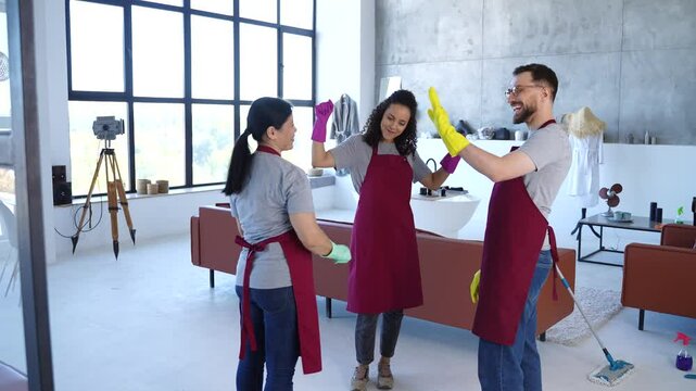 Cleaning team giving each other high five, celebrating outstanding results. Professional housekeepers finished work in modern house