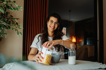One young beautiful caucasian woman wearing glasses and eating corn flakes or cereal for breakfast 