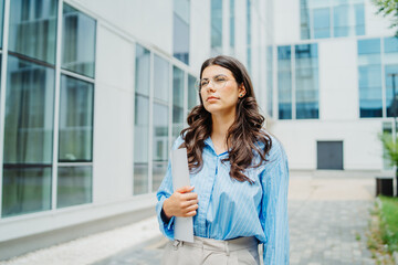 One beautiful young successful business woman going to work at business office modern building while holding papers and wearing glasses	