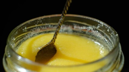Stirring ghee butter with a spoon on a black background.