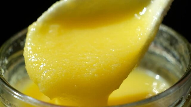 Fresh ghee oil pouring from spoon into jar, slow motion