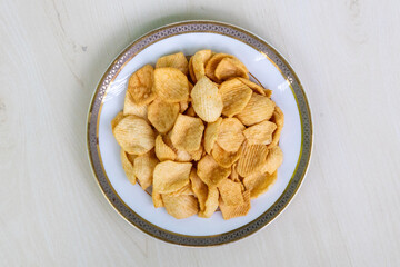 Delicious crispy potato crackers chips in a white plate on wooden background. Top view of crunchy tasty potato chips.