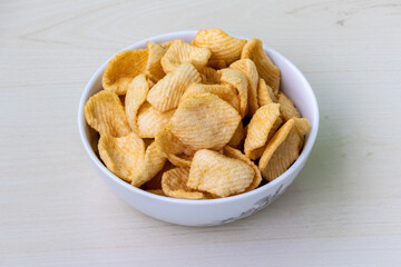 Tasty potato crackers chips in a white bowl on a light wooden background.