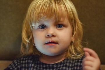 A little girl with blond hair is looking at the camera with fascination