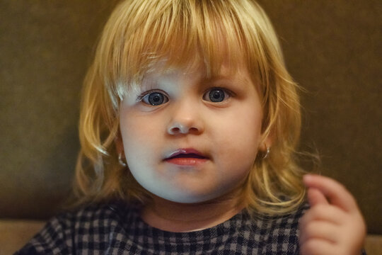 A little girl with blond hair is looking at the camera with fascination