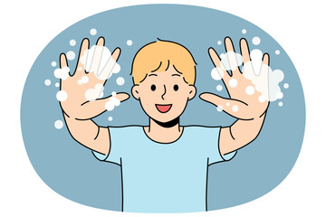 Little boy with foam shows soapy palms, recommending washing hands and following hygiene rules. Happy teenage boy doing preventive diseases and using soap after returning from school or walking