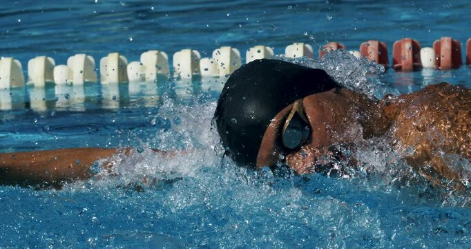 Super slow motion close up of young professional male swimmer with cap and goggles swimming with passion and motivation to achieve a victory in competition while practicing in swimming pool.