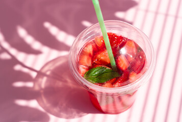Refreshing summer lemonade with strawberries on pink background with a beautiful shadows. Close-up. Selective focus.