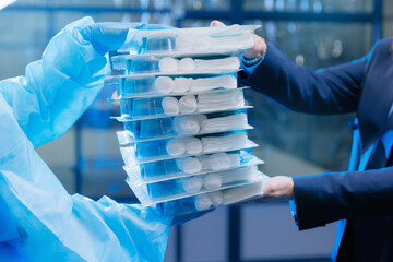 Businesswoman and doctor in protective suit holds sterile kits for surgery operations on blue factory background. Concept purchase of medical equipment and protective equipment vs virus