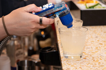 Female bartender hand adds carbonated fountain drinks to the alcohol cocktail drinks