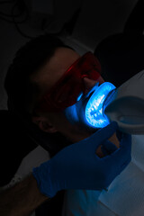 Patient whitens his teeth while treatment in dental cabinet. Ultraviolet teeth whitening procedure...