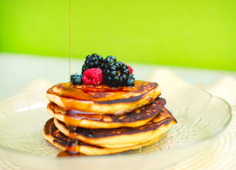 Plato de hot cakes o panqueques apilados con frutos rojos mientras le cae miel por encima 