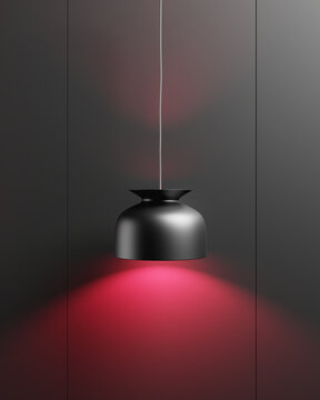 L&aacute;mpara colgante negra de dise&ntilde;o moderno, proyectando una luz roja sobre la superficie debajo de ella. El fondo es de color gris oscuro.