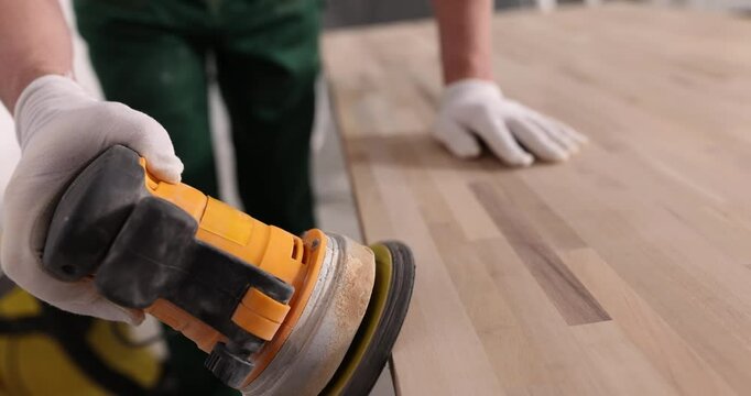 Worker in rubber gloves processes table wooden surface with grinding machine. Professional equipment for polishing parquet in apartment slow motion