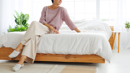 Web banner of mature woman in linen clothes sitting on bed at home