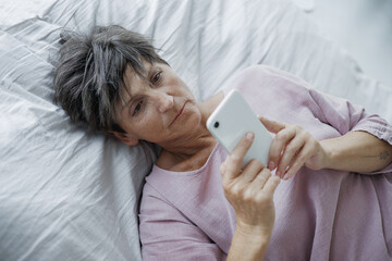 Top view of lonely mature woman using smartphone on bed