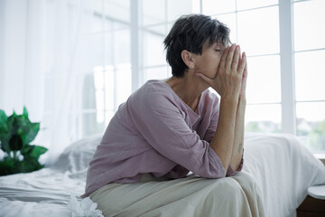 Lonely mature woman sitting near napkins on bed at home
