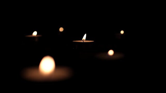 Round small candles in the dark. Lighting a candle, praying, hoping for the best. Religious atmosphere, candle fire on a black background