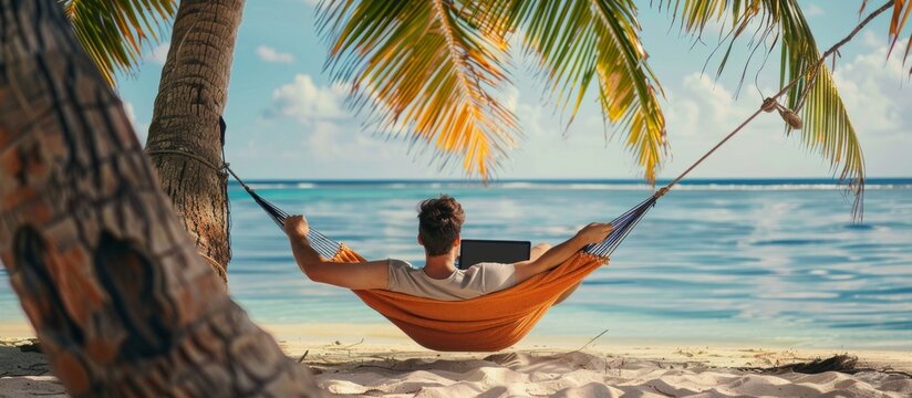 young man with laptop in summer in hammock on the beach