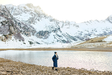 European woman stands by a mountain lake