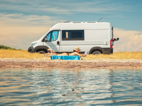 sea view to beauty girl that reads a book on sun chair in front of camper on the beach in hot summer day with nobody