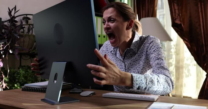 Crazy female employee yells in computer monitor suffering from hard burnout at workplace slow motion. Furious woman with nervous breakdown in office