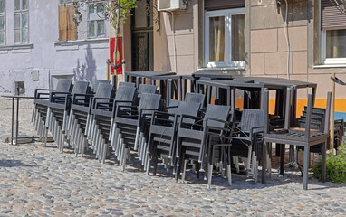 Stacks of Black Rattan Chairs and Tables in Front of Coffee Shop at Cobbled Street