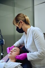 A beautician in pink gloves wipes a moisturizing mask from a girl's face with sponges.