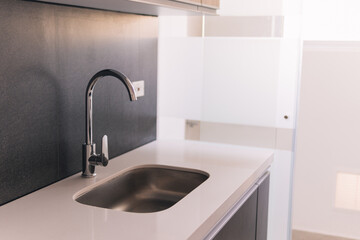 Sleek and modern kitchen sink area featuring a stainless steel faucet and minimalist design, set against a dark backsplash